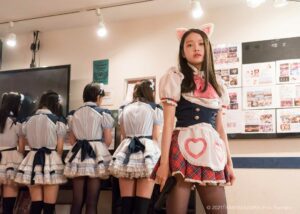 Baby assasins. A girl in a white skirt stands facing us with a gun whilst three other girls have their backs to us. Japanese Film Festival, Perth 2022