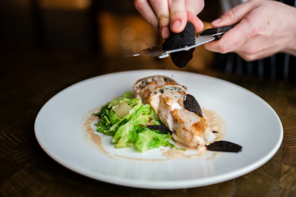 Caucasian hands shave truffle over a chicken breast on a white plate at The Rusty Fig Perth